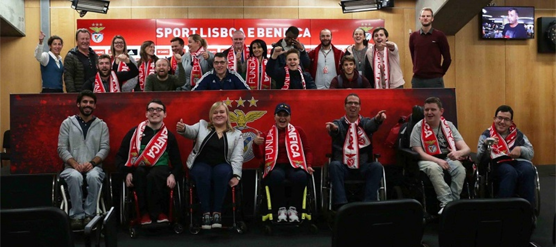 Football For all Teilnehmer*innen, teilweise im Rollstuhl, lachen freudig in die Kamera. Manche haben einen Fanschal von Lissabon um.