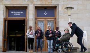 Ein Rollstuhlfahrer wird von Mitarbeiter*innen von RB Leipzig vor dem Eingang zu den Raum RB Leipzig Club Scouts begrüßt.