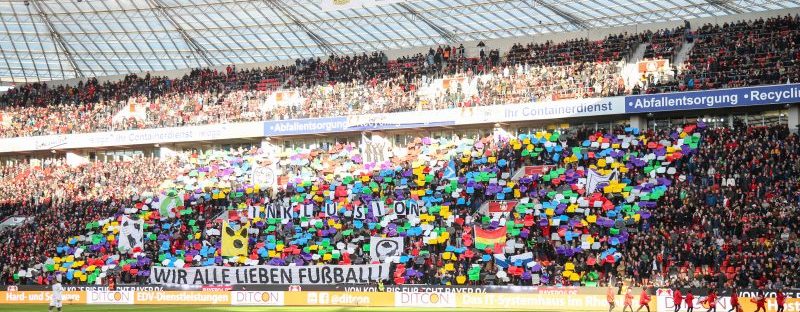Choreographie Inklusion von Bayer 04 Leverkusen: Viele bunte Fahnen, selbst gestaltete Symbole zu Inklusion und Schriftzug: Inklusion wir alle lieben Fußball werden hochgehalten.