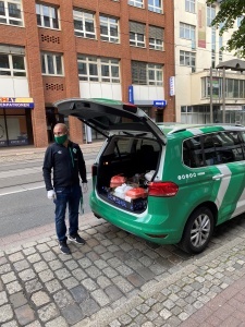 Ein Mann steht vor einem grünen Auto, welches mit Mahlzeiten beladen ist.