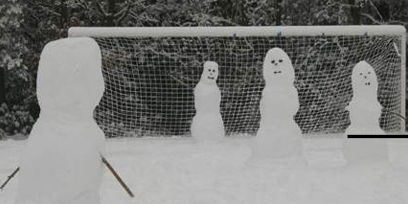 Vier Schneefiguren auf einem verschneiten Fußballfeld.