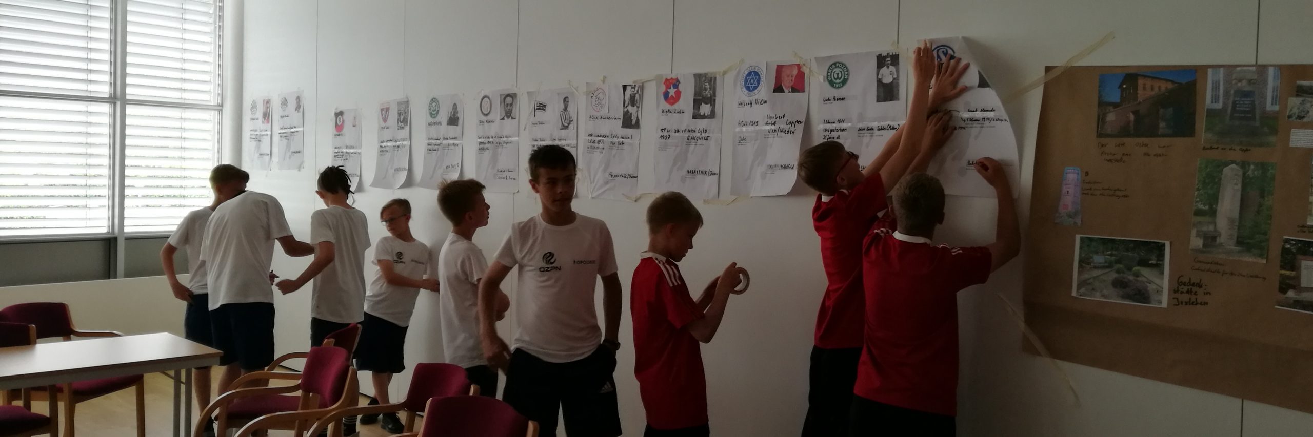 Jugendliche kleben auf Zetteln gestaltete überdimensionale Spielerpässe verfolgter Fußballer aus dem Nationalsozialismus an die Wand.