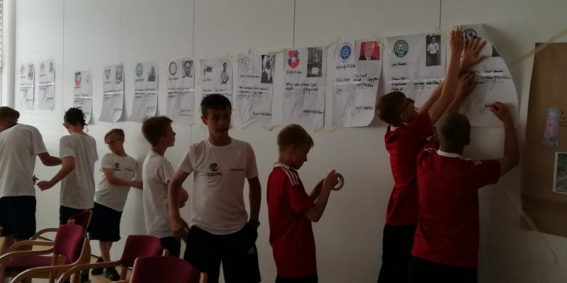 Jugendliche kleben auf Zetteln gestaltete überdimensionale Spielerpässe verfolgter Fußballer aus dem Nationalsozialismus an die Wand.