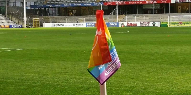 Eckfahne in Regenbogen-Farben mit Rasen und den Rängen des Dreisamstadions im Hintergrund.