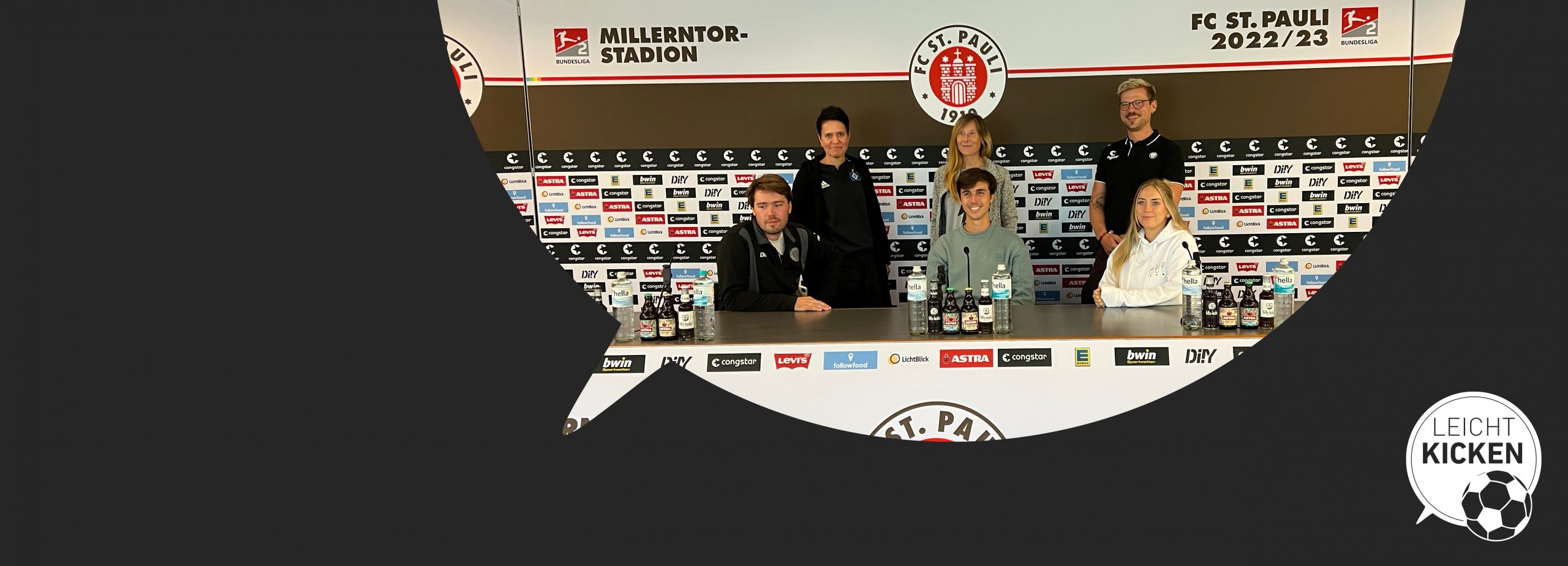 Alternativtext: Leicht Kicken-Gruppenfoto im Pressekonferenzraum des FC St. Pauli. Sechs Personen formieren sich hinter den drei Mikrofonen.