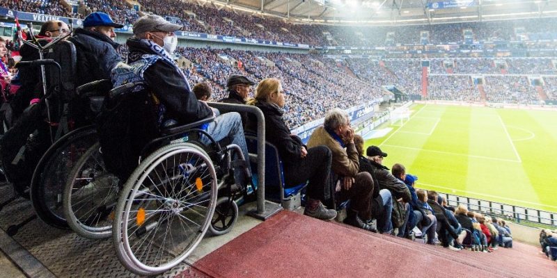Menschen mit Rollstuhl in der Veltins Arena mit Blick auf das Spielfeld.