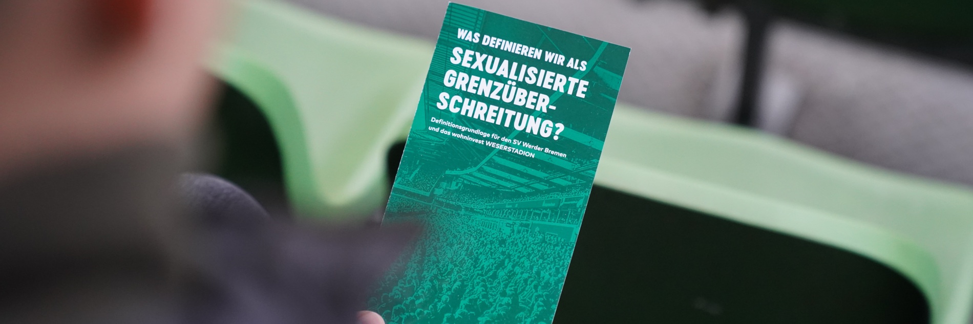 Person hält Flyer mit "Was definieren wir als sexualisierte Grenzüberschreitung?"-Schriftzug in der Hand.
