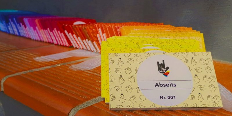 Kleine Heftchen liegen aufgereiht auf einer Treppe. Die Hefte sind dabei in verschiedenen Farben gehalten, so dass sie einen Regenbogen ergeben. Ganz vorne liegt ein gelbes Heft mit „Abseits“-Schriftzug und FlipKick-Logo.