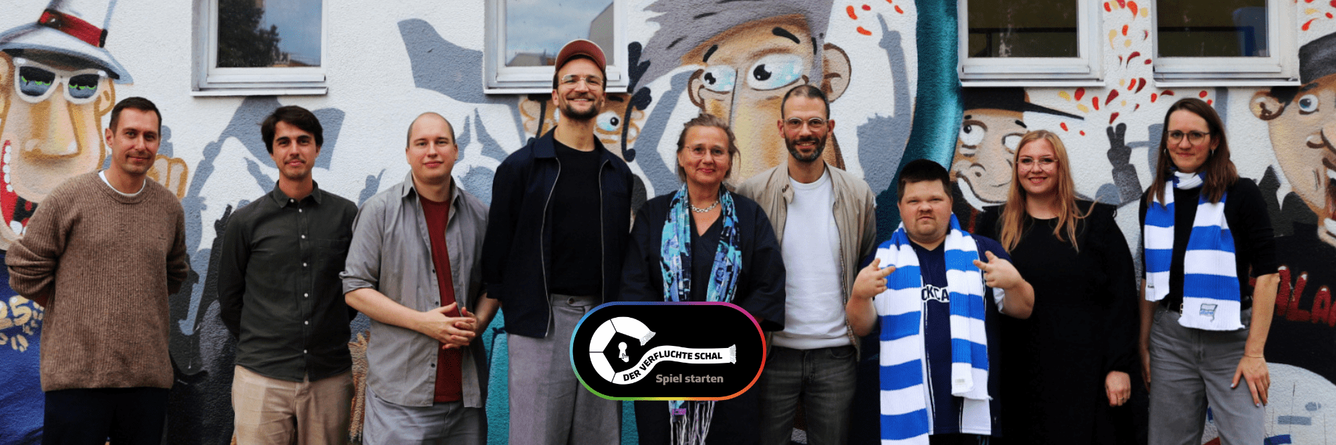9 Personen, die für ein Gruppenbild posieren. 2 Personen tragen einen blau-weißen Schal. In der Ecke ist das Projekt-Logo mit dem Text Klick4All – Alle ins Spiel bringen