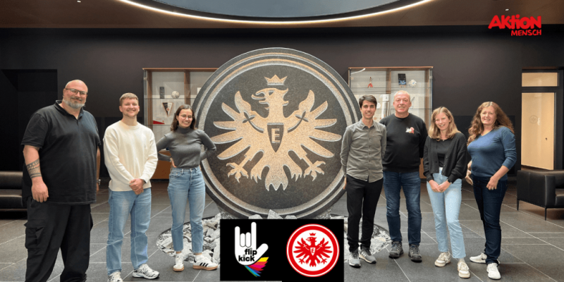 Gruppenbild vor großem Eintracht Logo. Logo FlipKick & SGE & Aktion Mensch