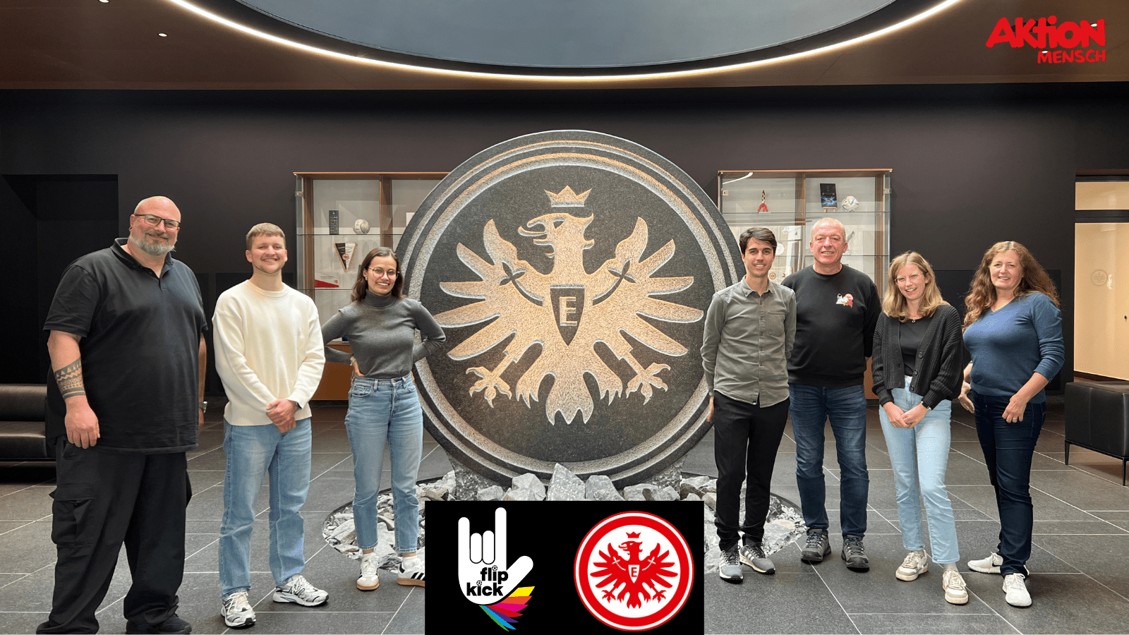 Gruppenbild vor großem Eintracht Logo. Logo FlipKick & SGE & Aktion Mensch