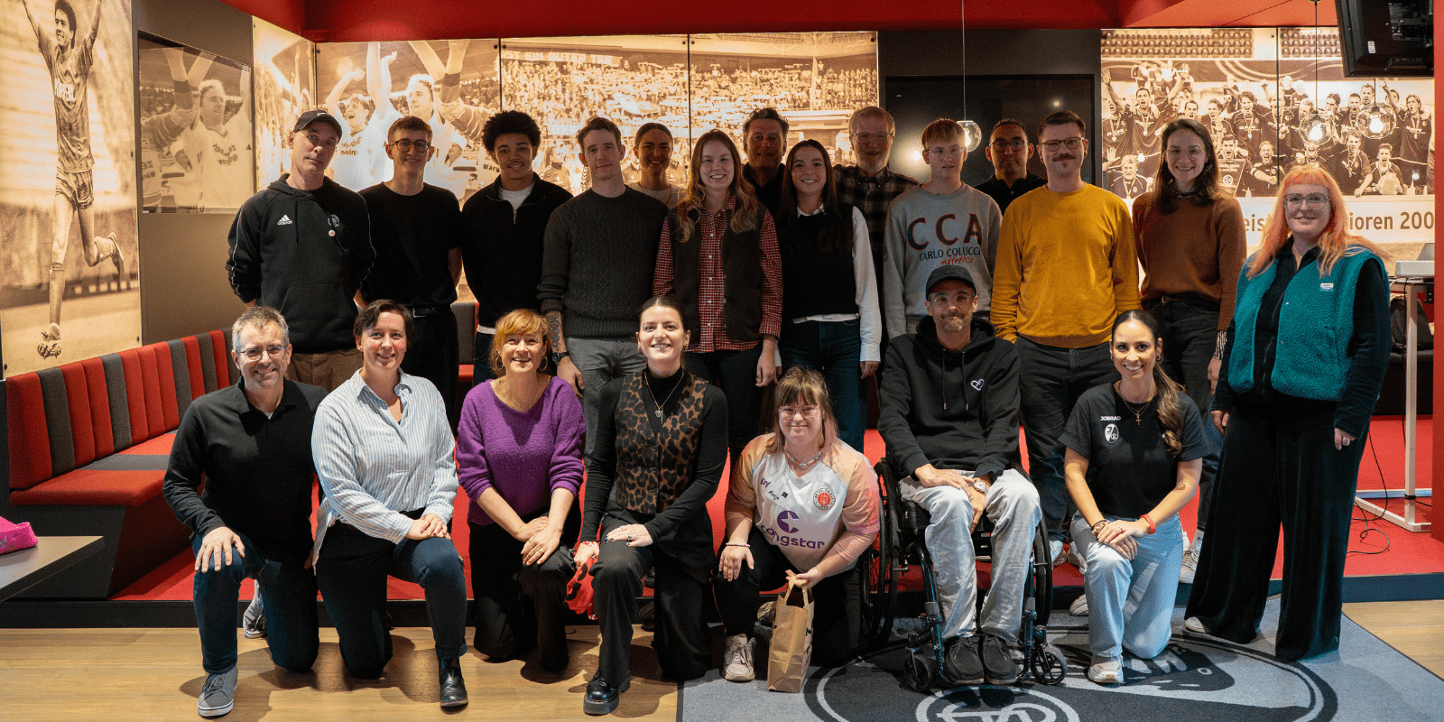Gruppenbild mit ganz unterschiedlich aussehenden Menschen. Hintere Reihe steht und die vorderer Reihe hockt/sitzt