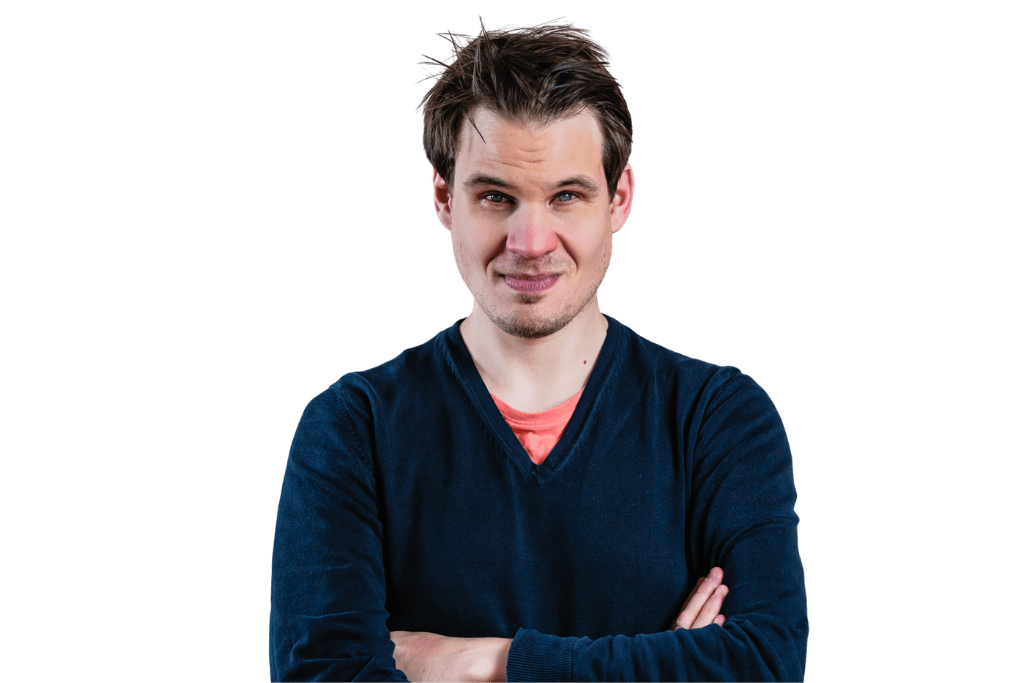 Jonas steht mit verschränkten Armen und lächelt in die Kamera. Er trägt einen Bart und eine zerfranste Frisur mit braunen Haaren.
