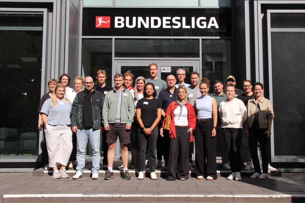 Gruppe von Erwachsenen vor dem Eingang der Bundesliga-Zentrale in Frankfurt mit sichtbarem Bundesliga-Logo über der Tür