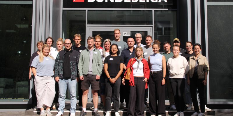 Gruppe von Erwachsenen vor dem Eingang der Bundesliga-Zentrale in Frankfurt mit sichtbarem Bundesliga-Logo über der Tür